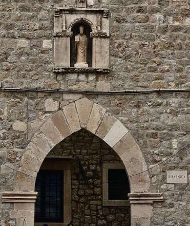 Brown/gray granite statue of Saint Blaise standing over an entrance to Dubrovnik in an alcove
